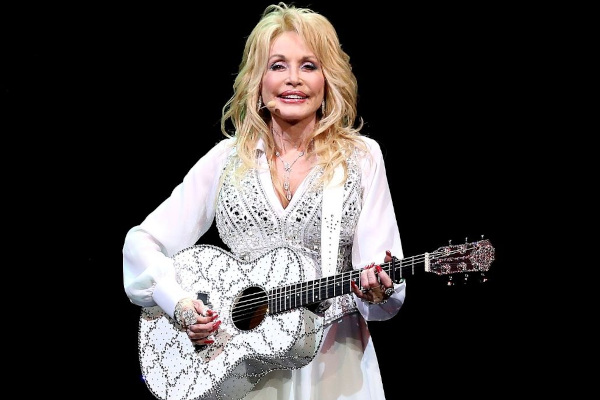 Dolly Parton com violão e roupas brancas brilhosas